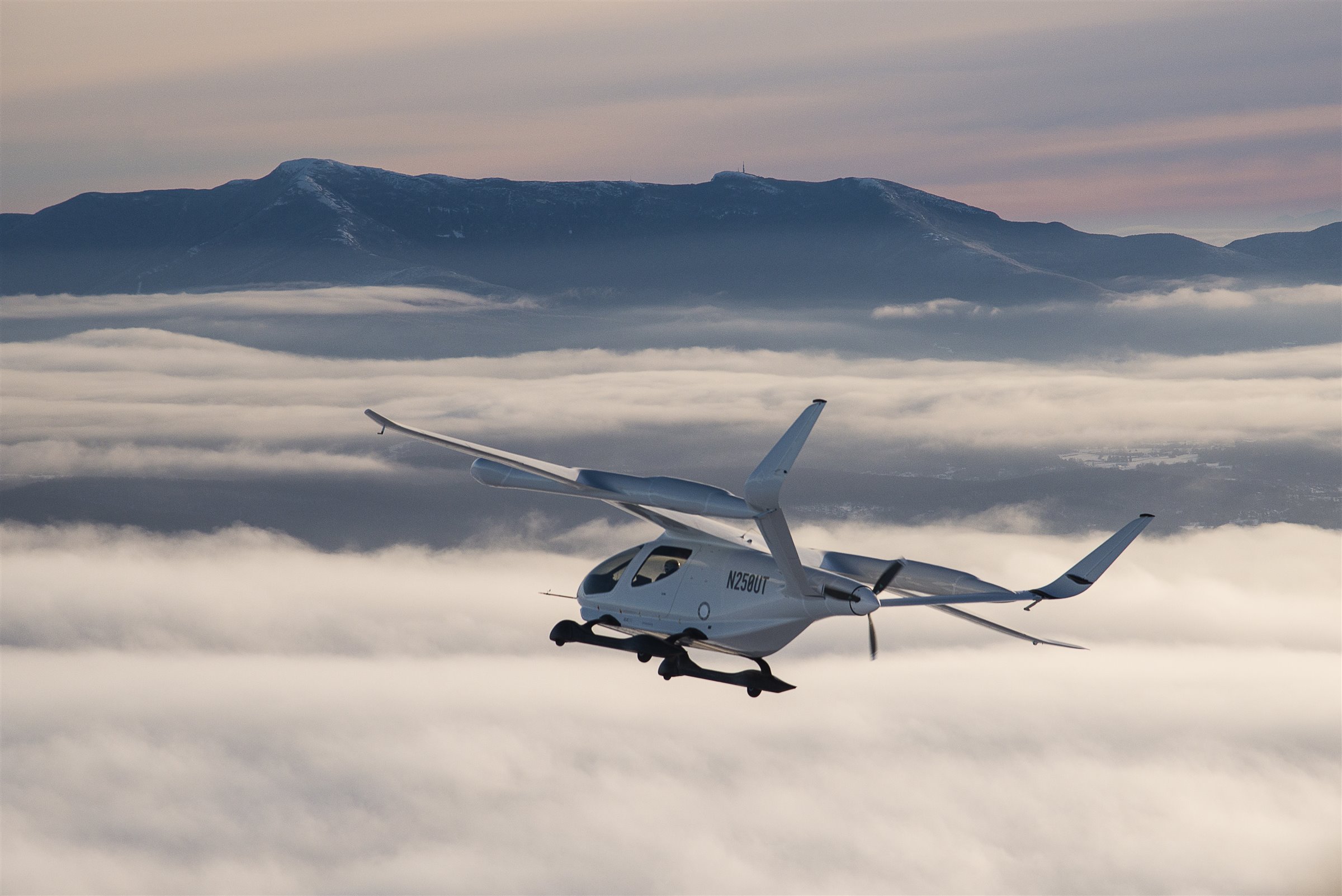 Electric aircraft flying above clouds and mountains